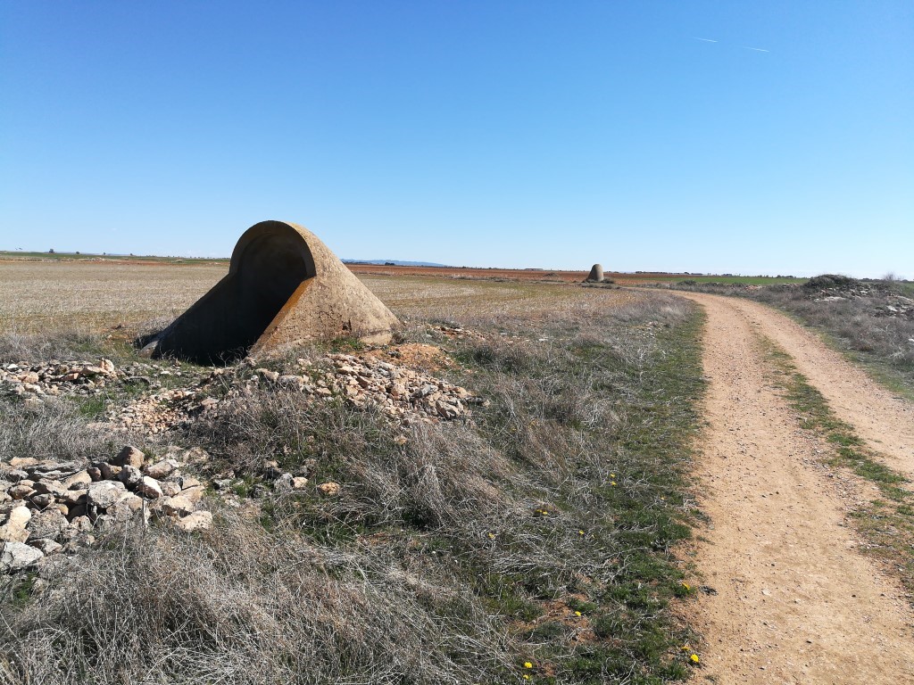 Boca de acceso a un refugio antiaéreo junto a terrenos agrícolas.